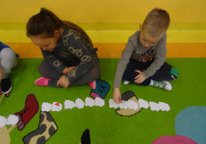 Dwoje dzieci przelicza szablony mapy Polski ułożone w szeregu, odwracają piąty z kolej.